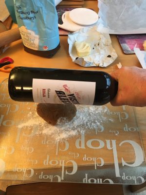 Hand holding a wine bottle above gingerbread dough, ready to flatten it